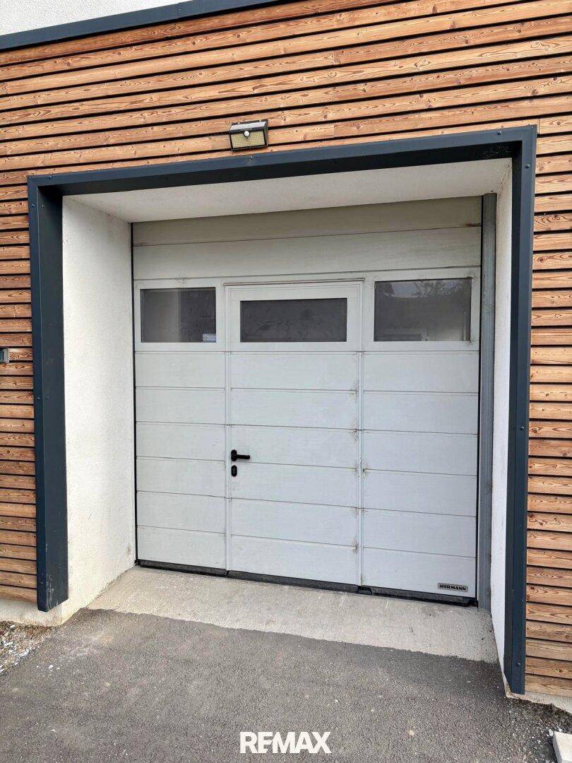 Moderne Garagentür mit Fenstern, eingebettet in eine Fassade mit horizontaler Holzverkleidung.