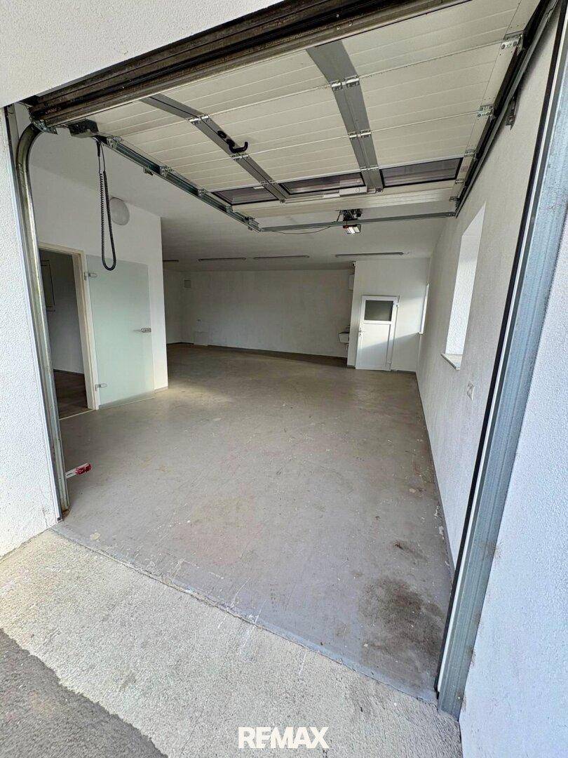 Geräumige Garage mit Betonboden, weißen Wänden und einem großen Sektionaltor mit Oberlichtern.
