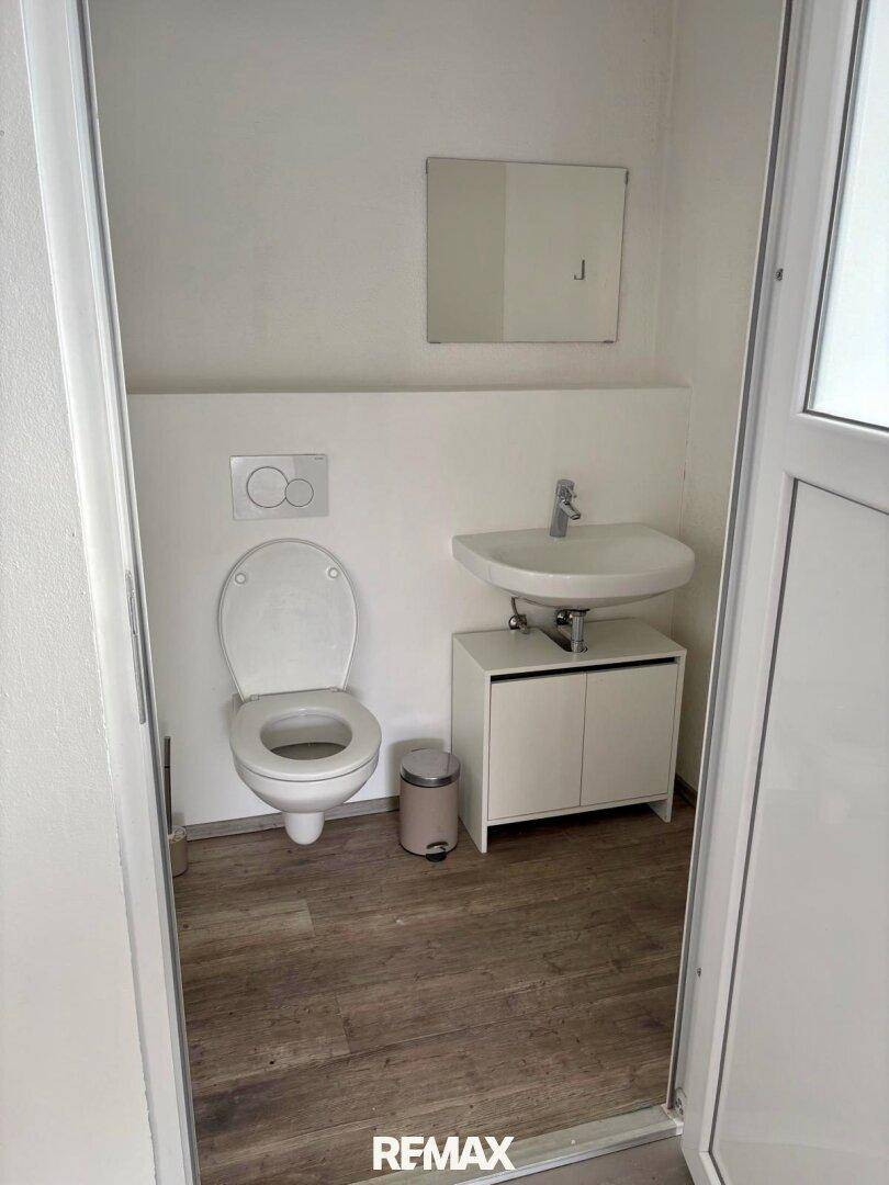 Kleine, saubere Toilette mit wandhängendem WC, Waschbecken mit Unterschrank und einem Spiegel.