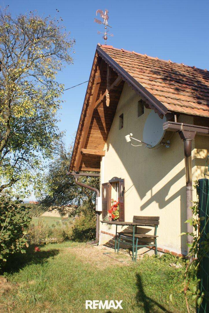 Seitenansicht eines traditionellen Hauses mit Ziegeldach, Fensterläden und einer kleinen Bank.