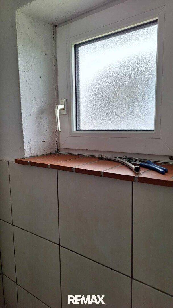Badezimmerfenster mit Milchglas und gefliester Fensterbank, sorgt für Privatsphäre und Licht.