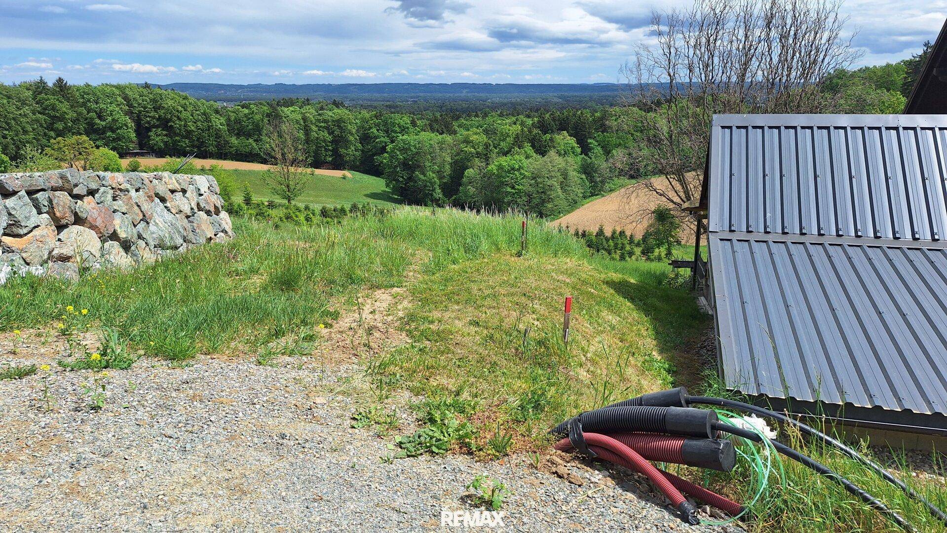 Blick auf ein Gebäude mit Solaranlage und eine Steinmauer vor einer weiten grünen Landschaft.