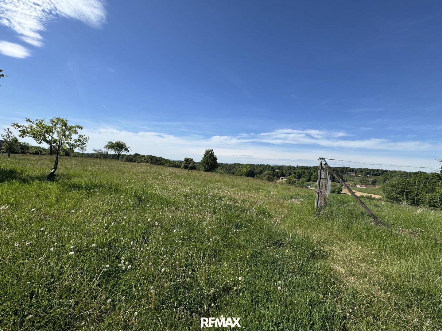 Eine grasbewachsene Hügellandschaft mit einem Zaun, die einen weiten Blick auf Felder und Häuser bietet.