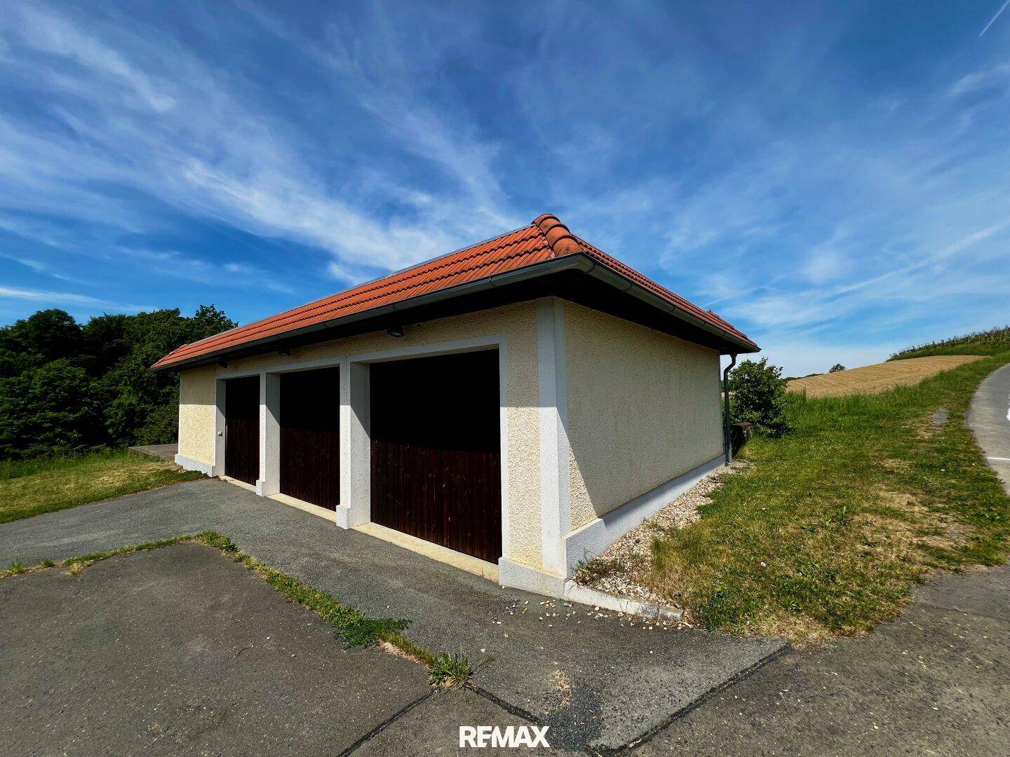 Separate Garage mit drei Stellplätzen, roten Ziegeln und asphaltierter Zufahrt.