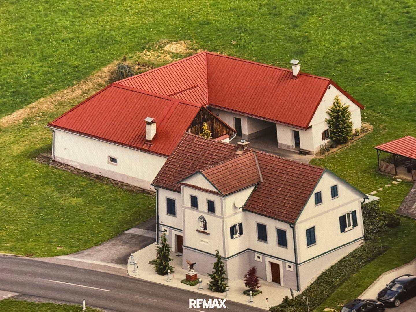 Vogelperspektive der beiden Gebäude mit roten Dächern, umgeben von grünen Wiesen und einer Straße.