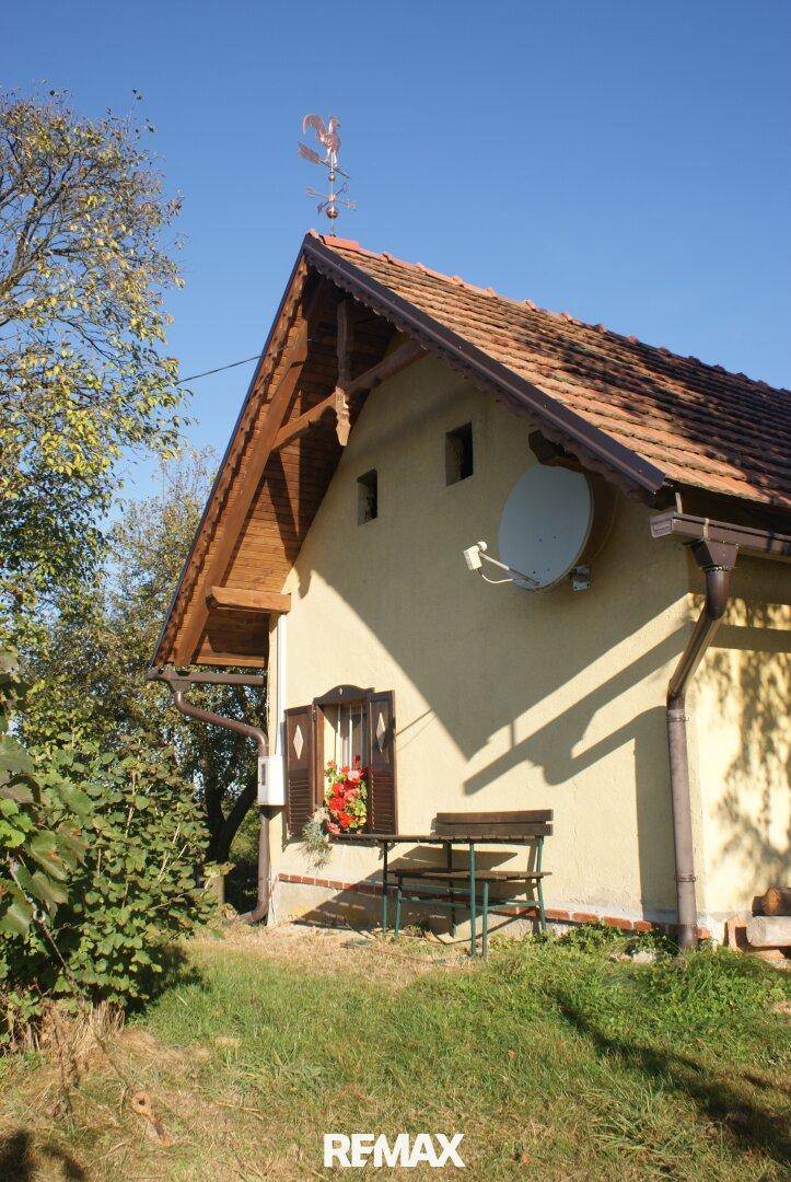 Seitenansicht eines traditionellen Hauses mit Ziegeldach, Fensterläden und einer kleinen Bank.
