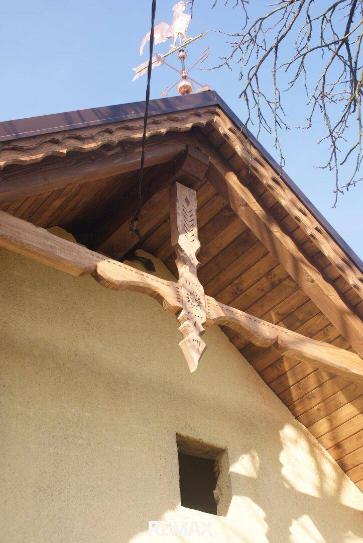 Detailansicht des Daches mit Holzschnitzereien und einem Wetterhahn unter blauem Himmel.