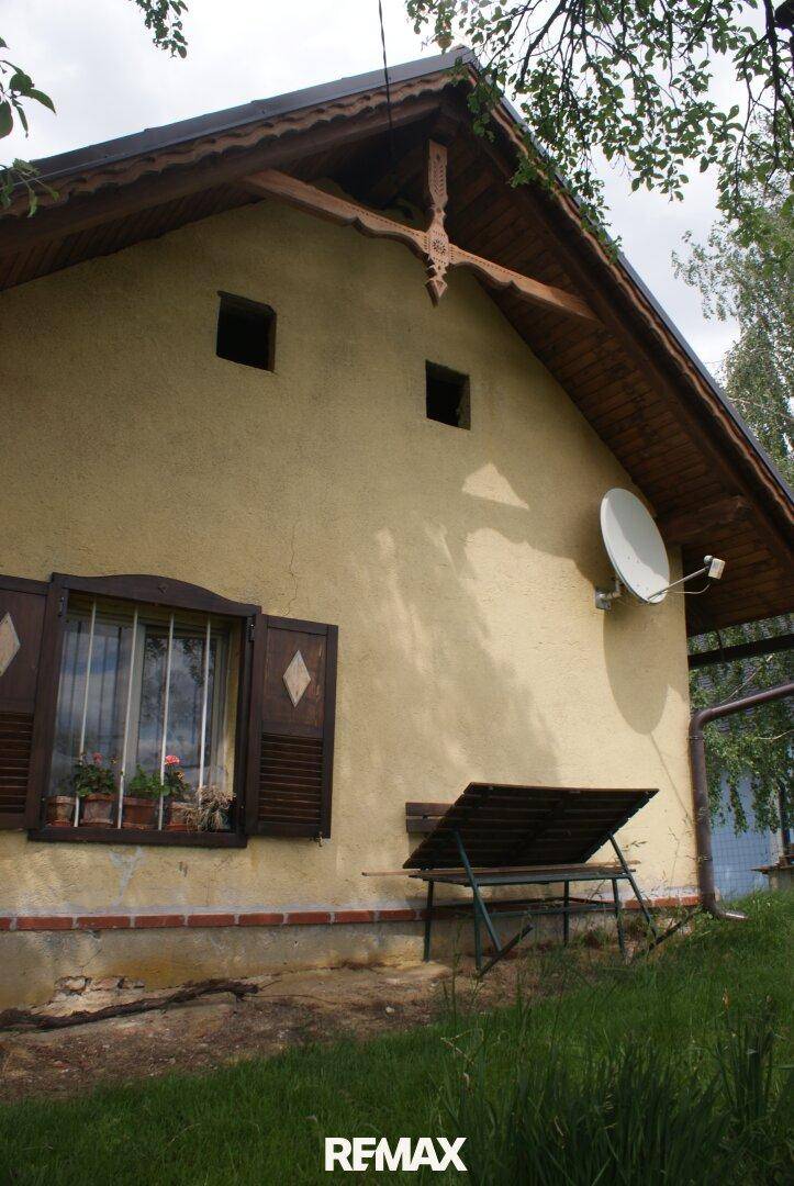 Seitenansicht des Hauses mit traditionellen Fensterläden und einer Satellitenschüssel an der Wand.
