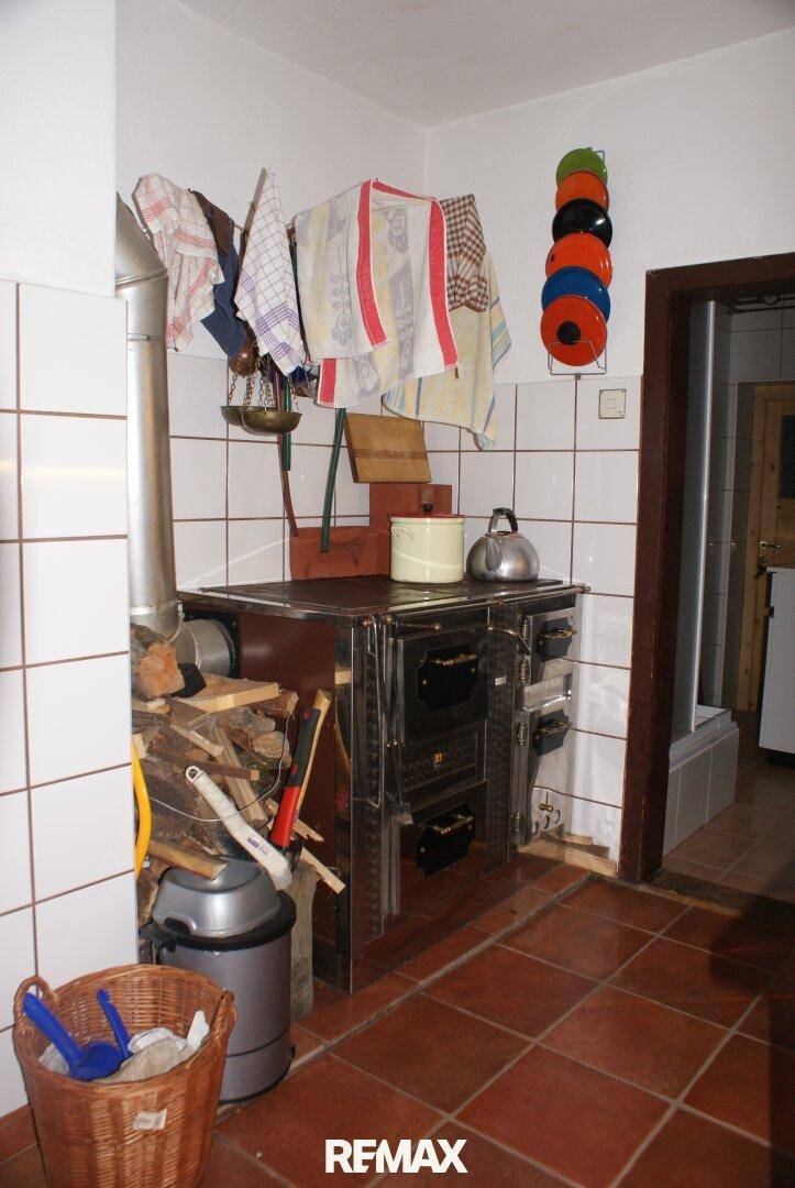 Rustikale Küche mit einem Holzofen, Terrakotta-Fliesenboden und weiß gefliesten Wänden.