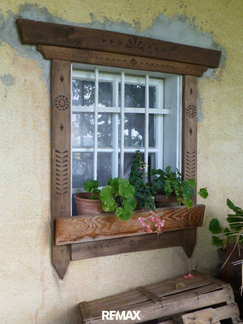 Detailansicht eines Fensters mit Holzrahmen, Sprossen und Blumenkästen.
