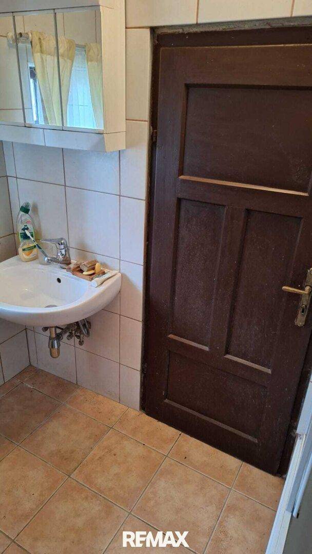Kleines Badezimmer mit Waschbecken, Spiegelschrank und hellen Fliesen an Wänden und Boden.