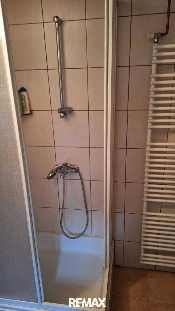 Duschkabine in einem Badezimmer mit hellen Fliesen und einem praktischen Handtuchheizkörper.
