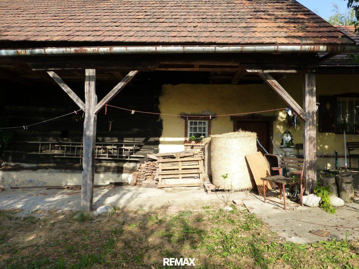 Überdachter Bereich an der Hausseite mit Holzkonstruktion und gelagertem Material.