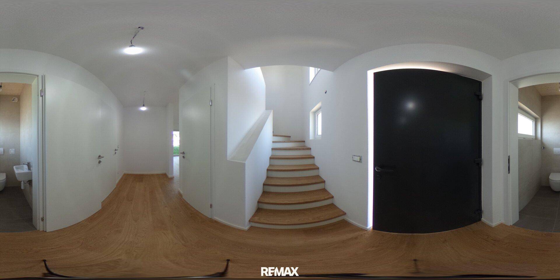 Panoramaaufnahme eines hellen Flurs mit Holztreppe und Zugang zu weiteren Räumen.