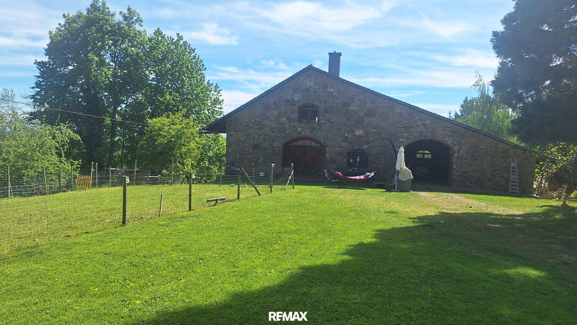 Rustikales Steingebäude mit großem Rasenbereich und Schaukelstuhl im Freien unter blauem Himmel.