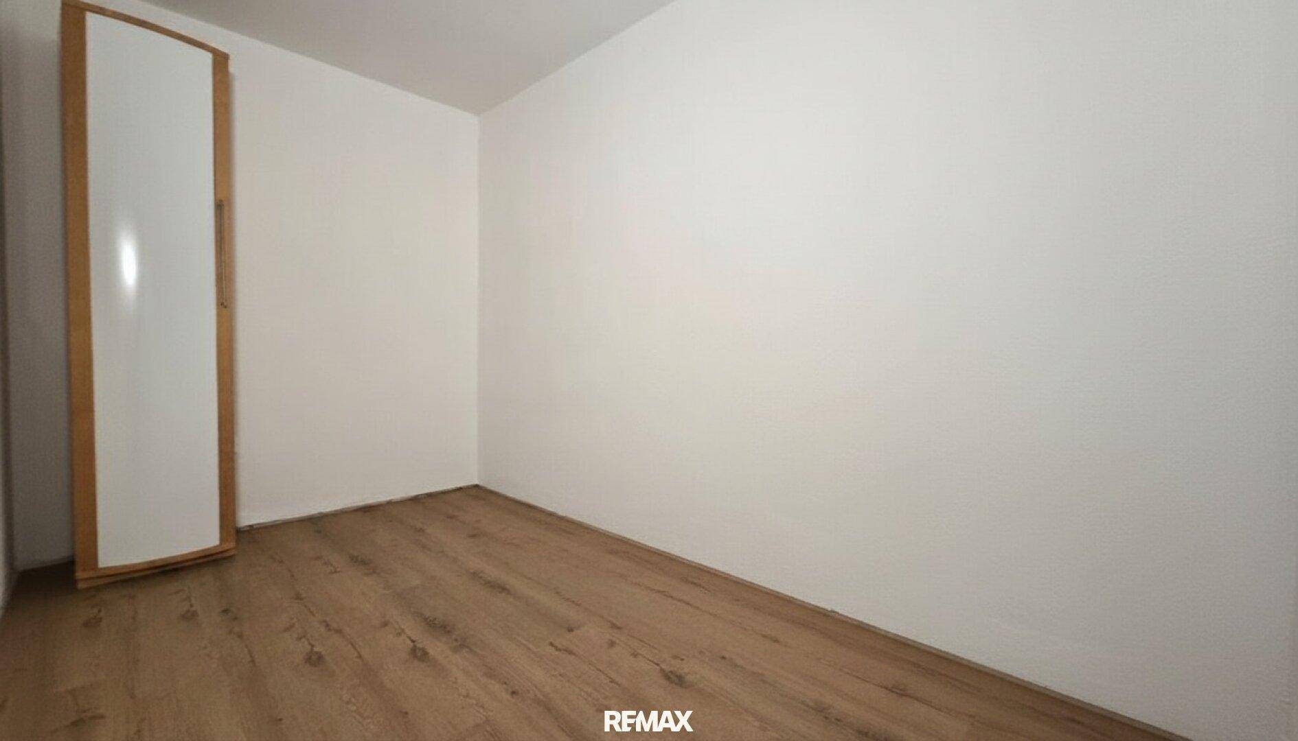Leeres Zimmer mit Laminatboden und weißen Wänden, bereit zur individuellen Einrichtung.