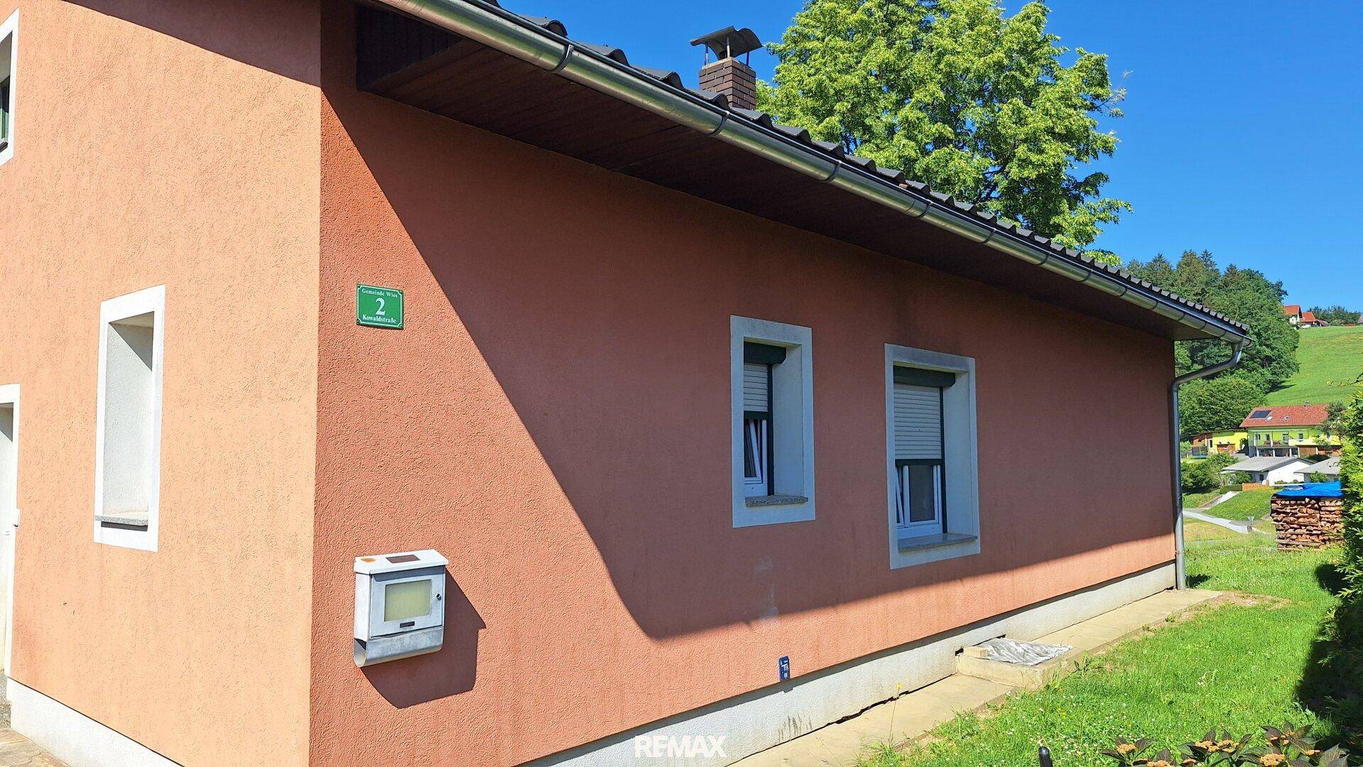 Seitenfassade des Hauses mit kleinen Fenstern, Rollläden und einem Briefkasten.