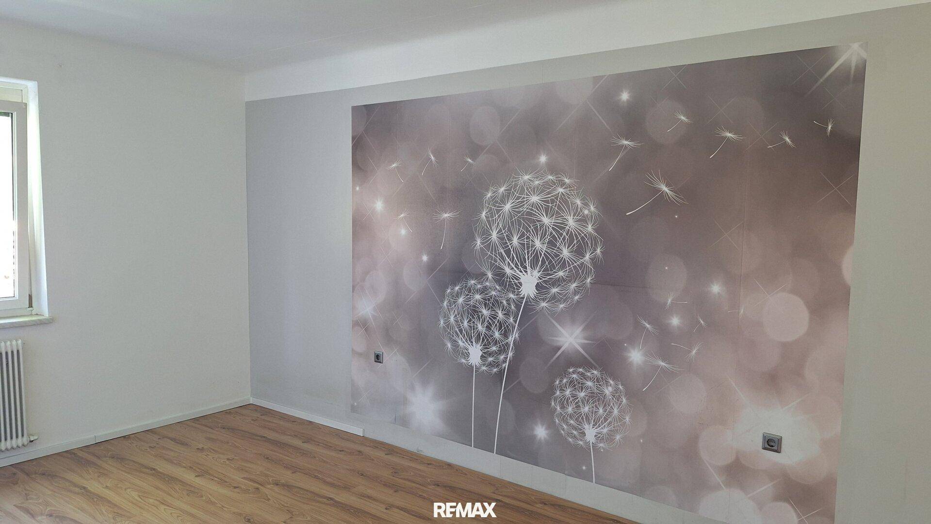 Zimmer mit Holzboden und einer Wand mit dekorativer Pusteblumen-Tapete.