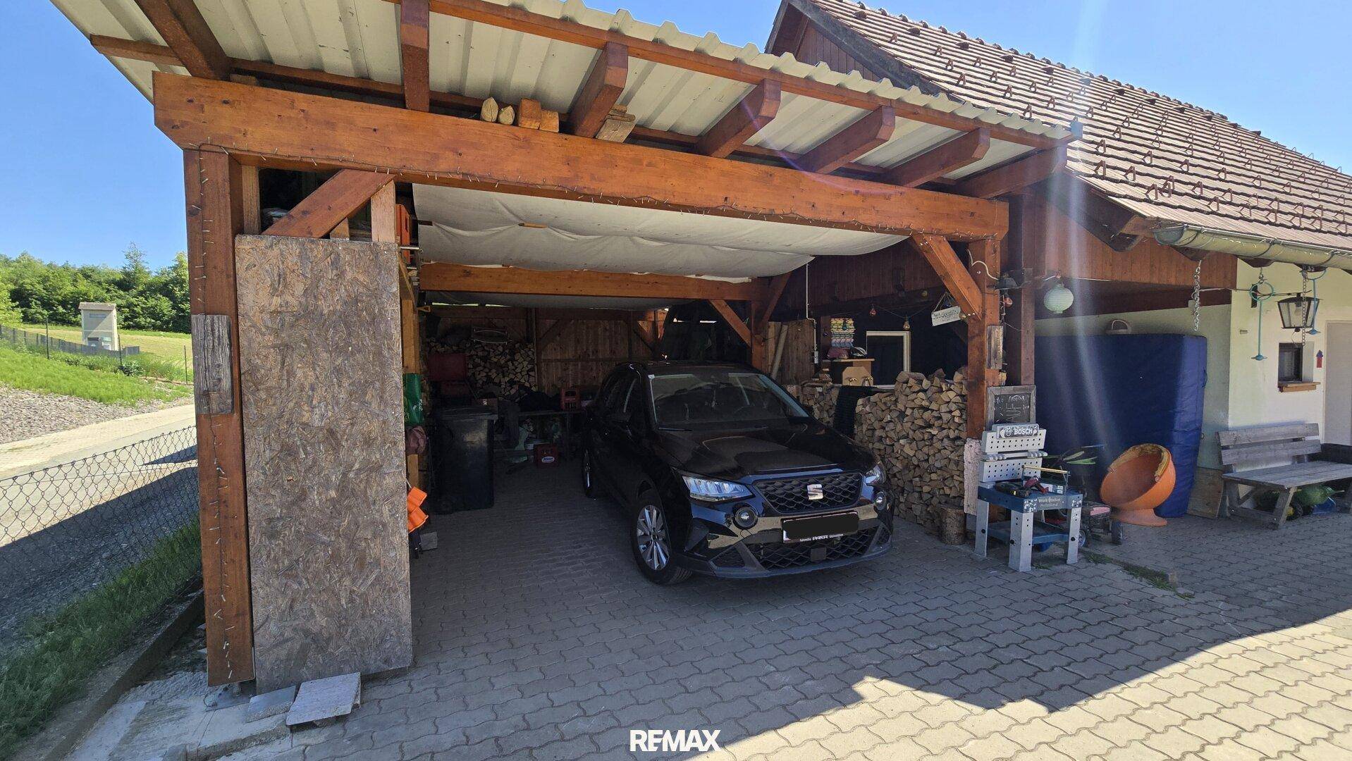 Überdachter Carport-Bereich mit Holzbalken, Stellplatz für ein Fahrzeug und Lagerfläche.