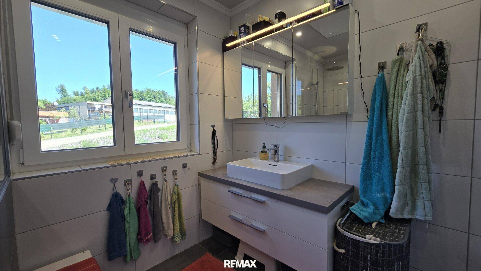 Modernes Badezimmer mit großem Fenster, Einzelwaschbecken und Spiegelschrank.
