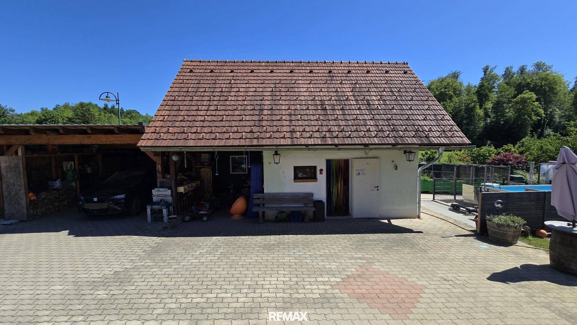 Nebengebäude mit Ziegeldach, gepflastertem Vorplatz und angrenzendem Carport.