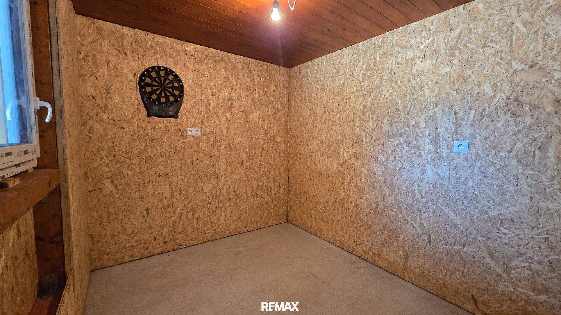 Kleiner Raum mit OSB-Platten an den Wänden und einem Dartboard.