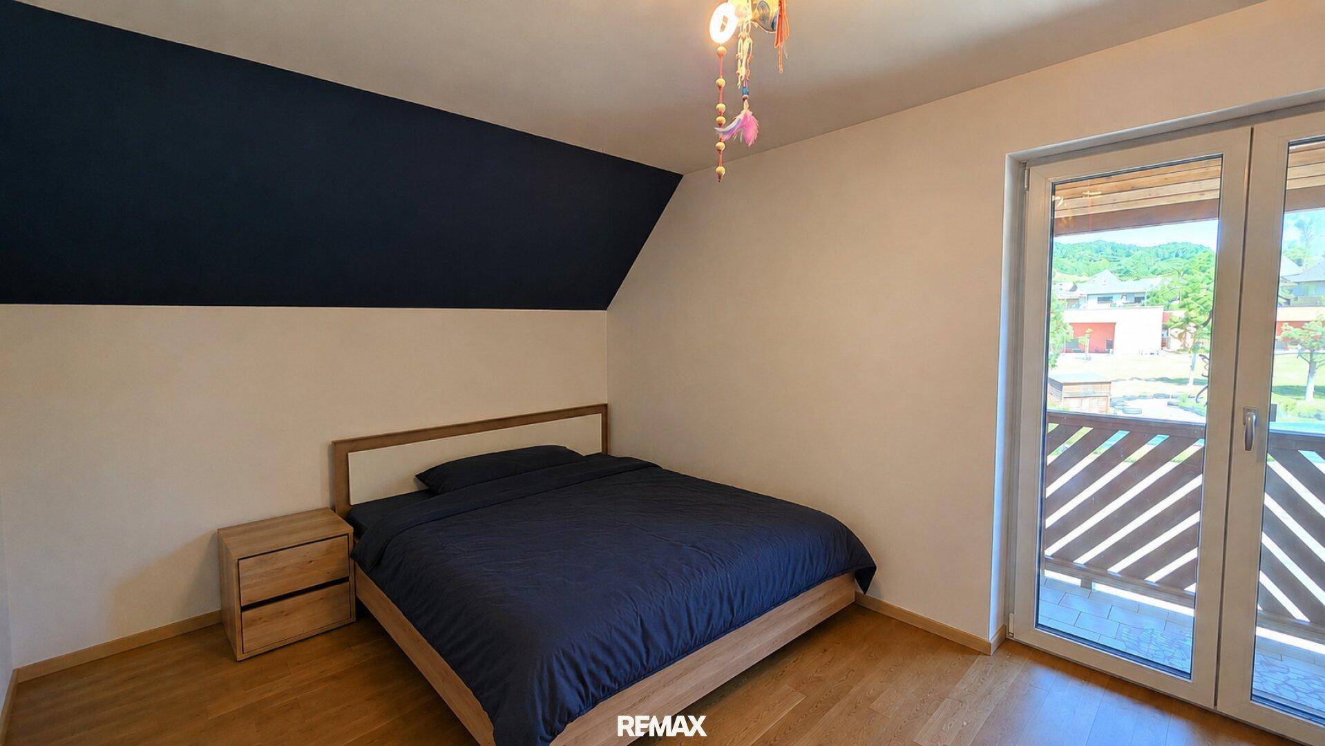 Schlafzimmer mit Holzboden, dunkler Akzentwand und direktem Zugang zum Balkon.