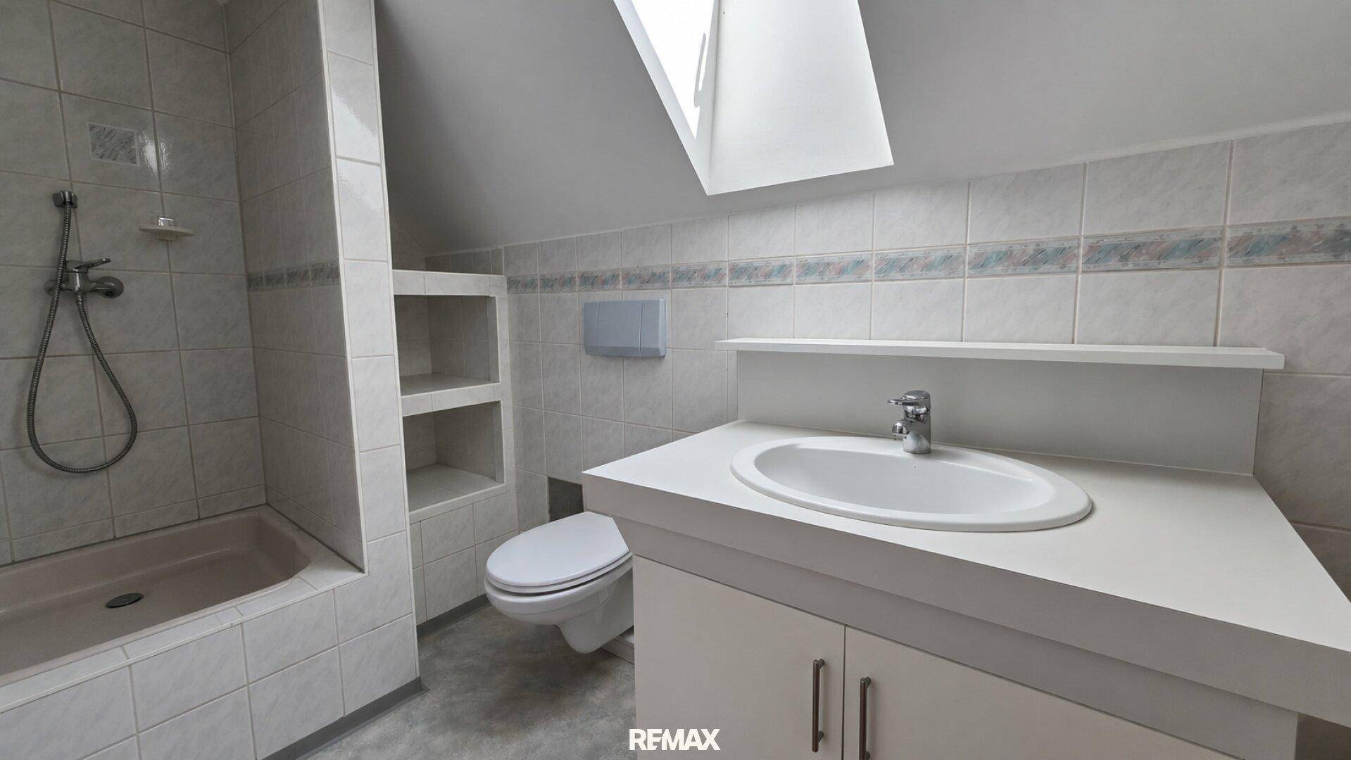 Badezimmer im Dachgeschoss mit Schrägdach, Dachfenster, Dusche und Waschtisch.