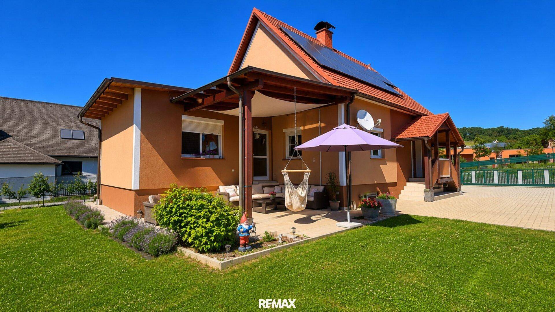 Gemütliche überdachte Terrasse mit Sitzgelegenheiten und Rasenfläche neben dem Einfamilienhaus.