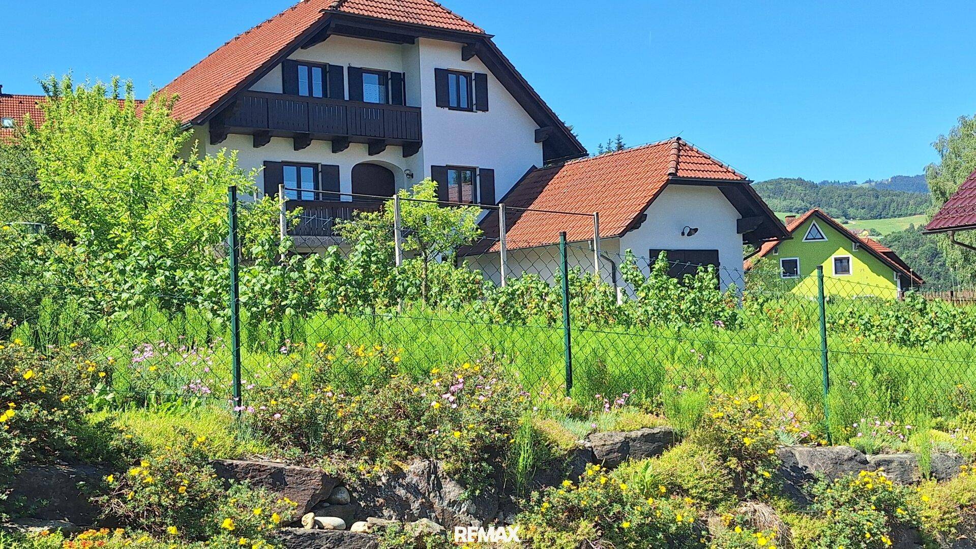 Charmantes Einfamilienhaus mit rotem Ziegeldach und grüner Umgebung, eingebettet in die Landschaft.