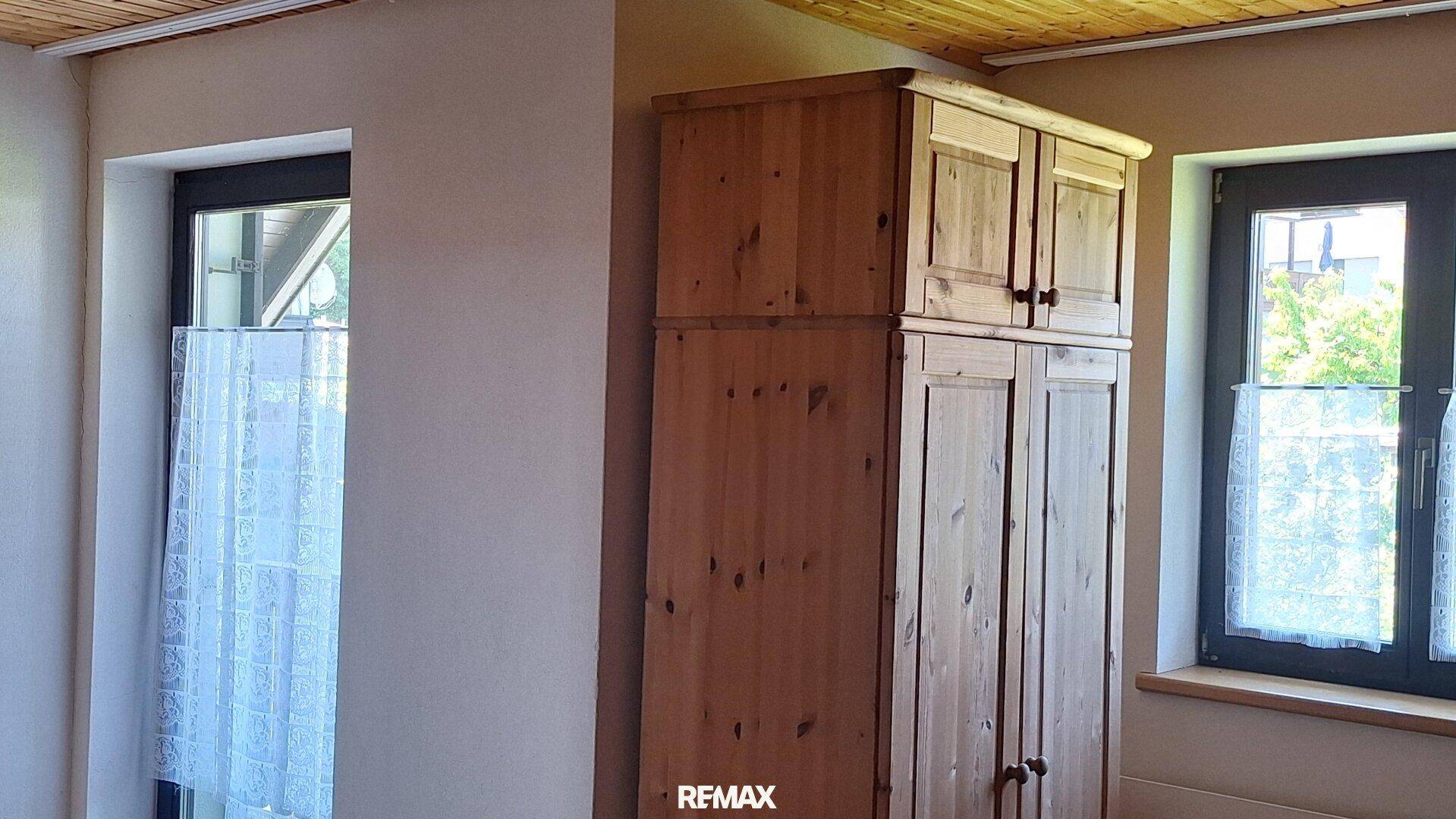 Schlafzimmer mit rustikalem Holzschrank, Holzdecke und zwei Fenstern, hell und funktional.