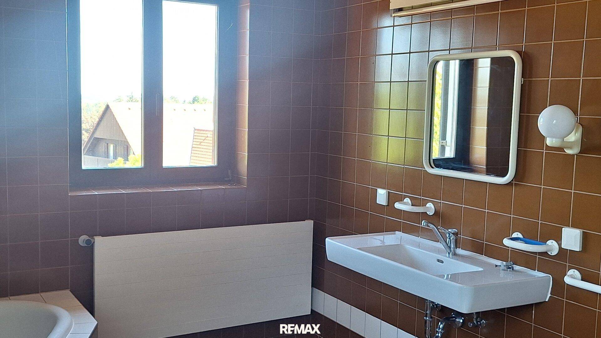 Badezimmer mit braunen Fliesen, modernem Waschbecken und Fenster, im Stil der 80er Jahre.