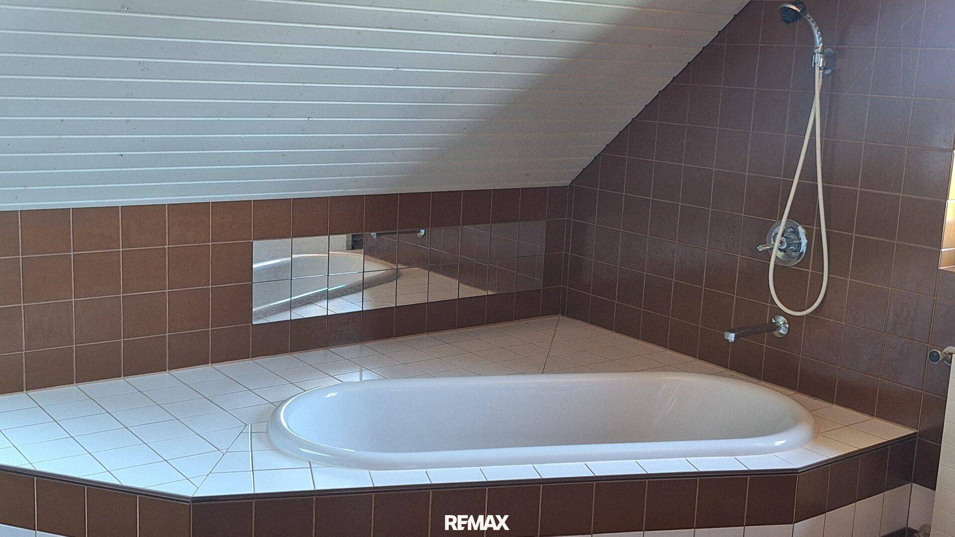 Badezimmer mit eingebauter Eckbadewanne und braunen Fliesen unter einer Dachschräge.
