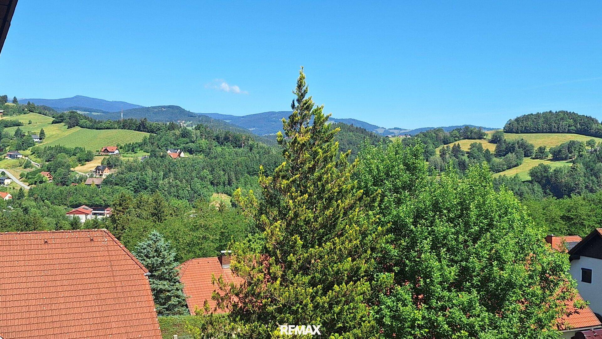 Weitläufiger Panoramablick über grüne Hügel und Berge unter blauem Himmel, eine malerische Landschaft.