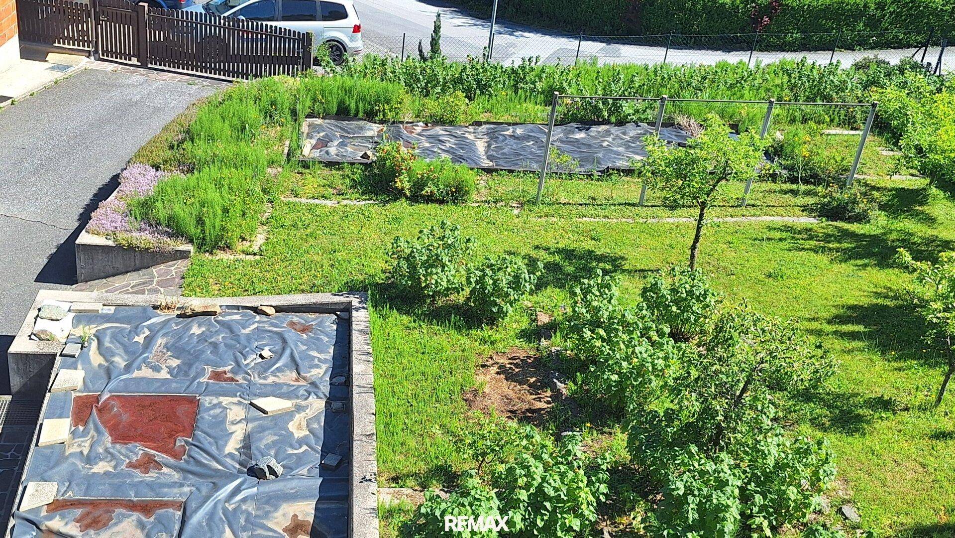Großer Gartenbereich mit Rasenflächen, Sträuchern und vorbereiteten Beeten, umgeben von Natur.
