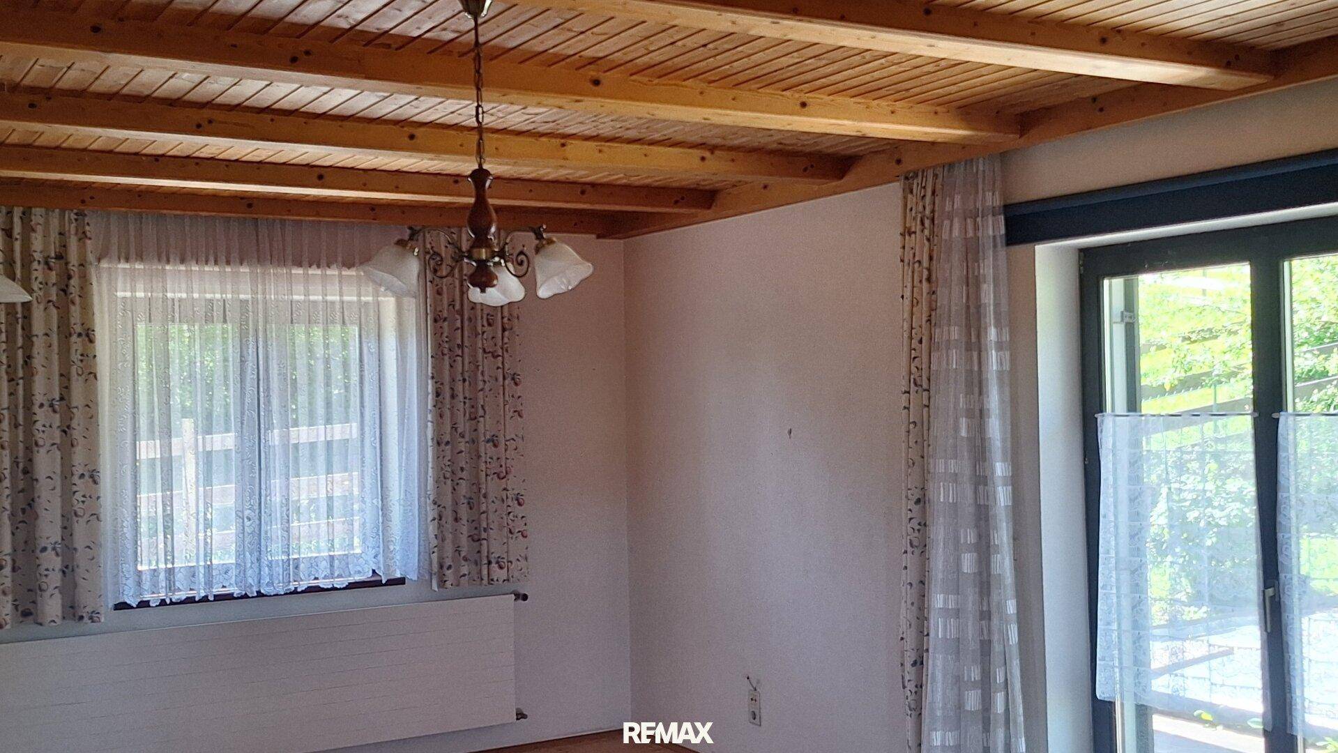 Gemütlicher Raum mit Holzdecke, großen Fenstern und traditioneller Hängelampe, hell und einladend.