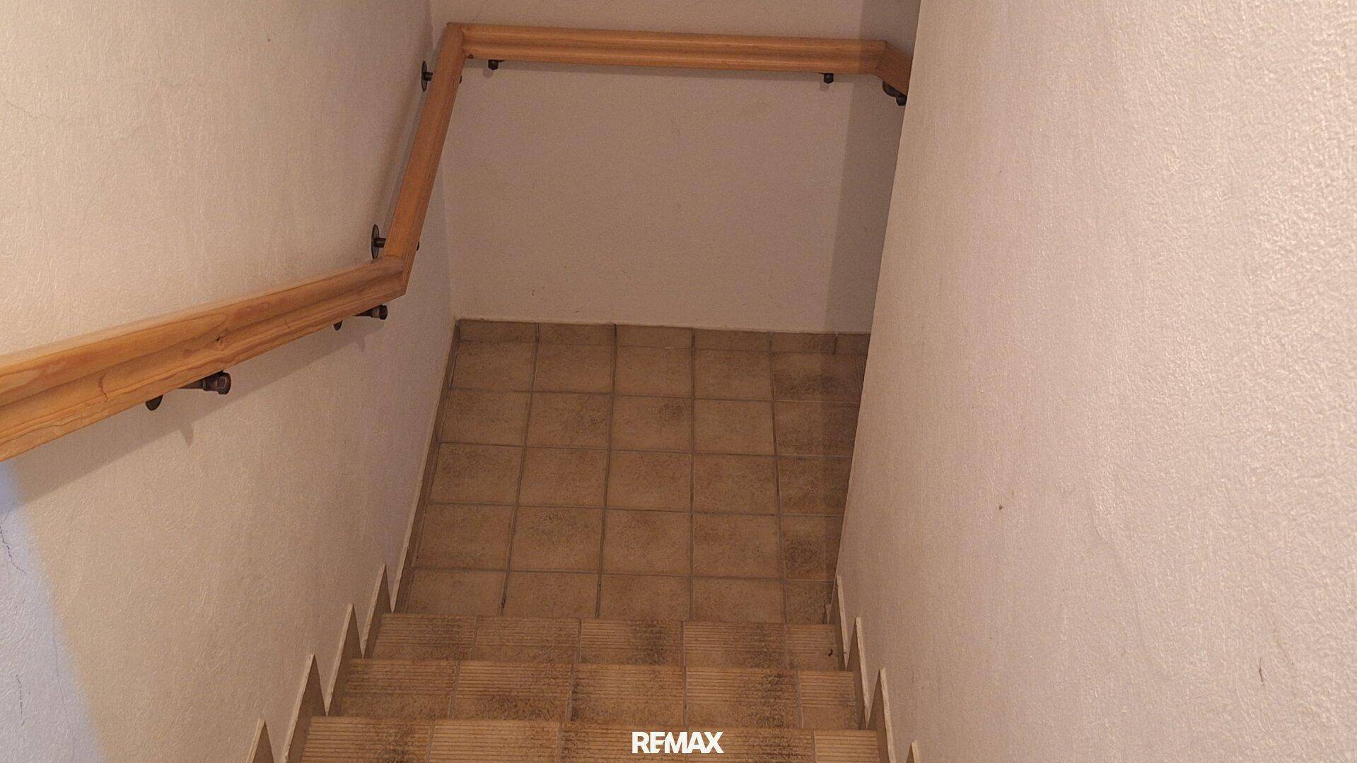 Treppenabgang mit Holzgeländer und gefliestem Boden, der in den unteren Bereich führt.