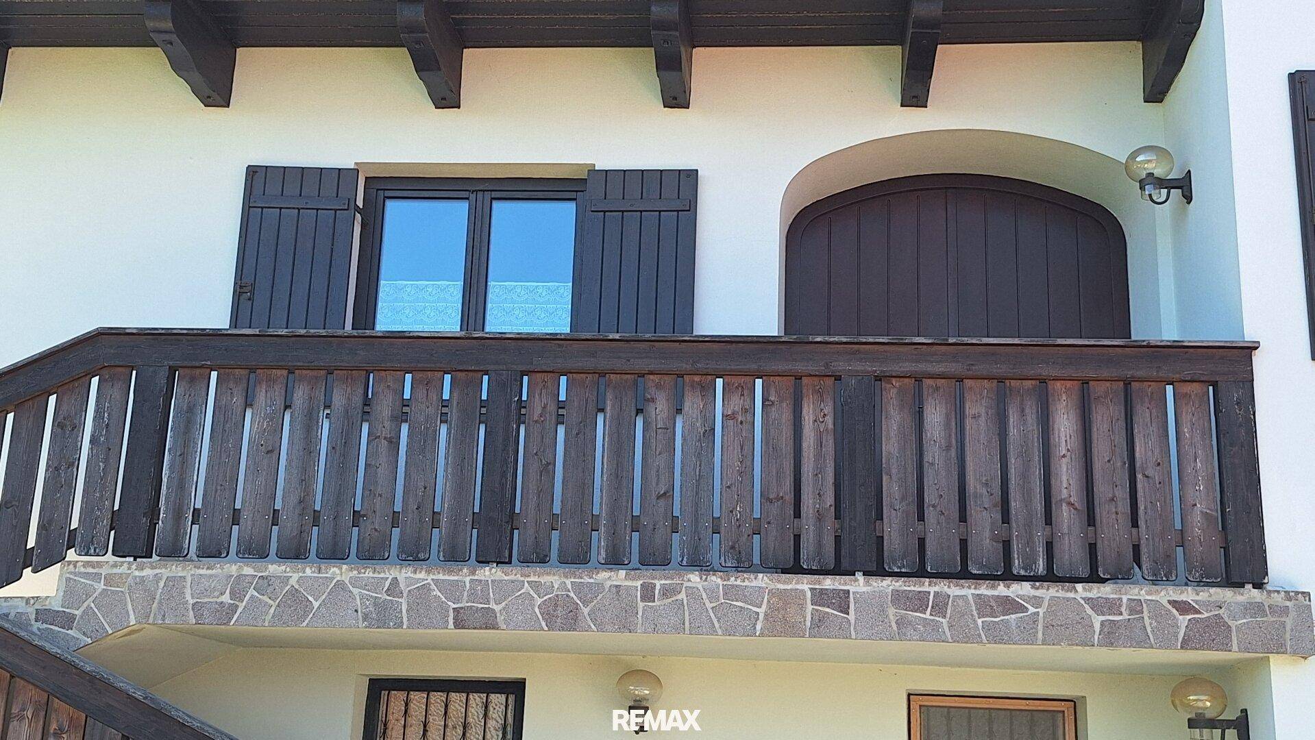 Traditioneller Holzbalkon mit Geländer und Steinverkleidung an der Fassade, gut erhalten.