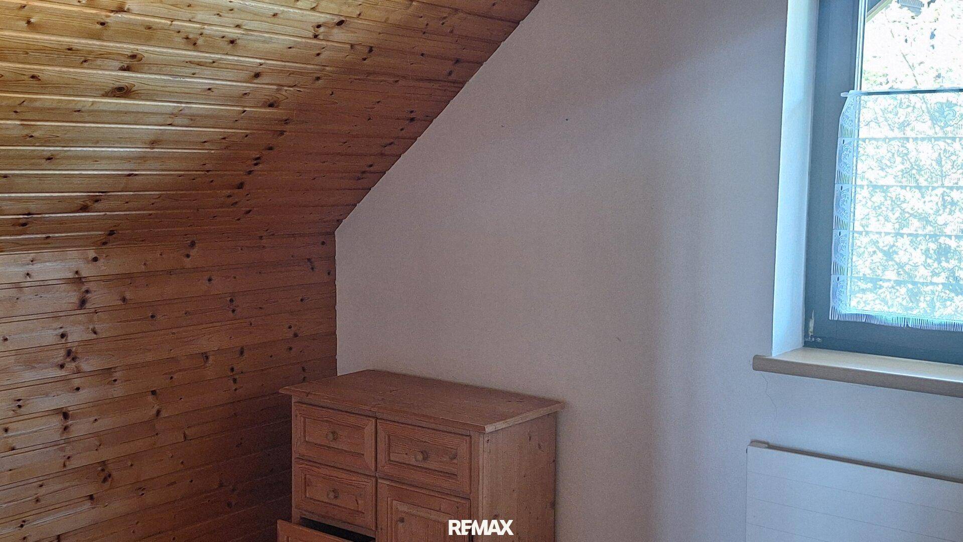 Dachzimmer mit Holzvertäfelung, Dachschräge und rustikaler Kommode, gemütlich und hell.