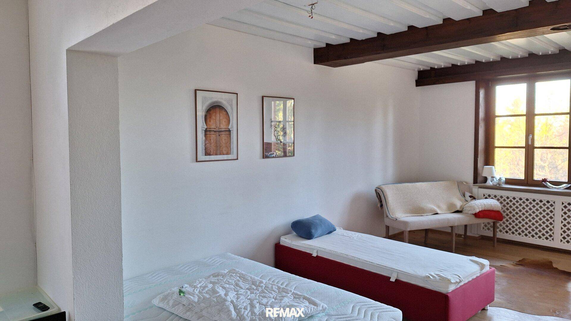 Schlafzimmer mit zwei Betten, Holzbalkendecke und Fenster mit Blick ins Grüne.