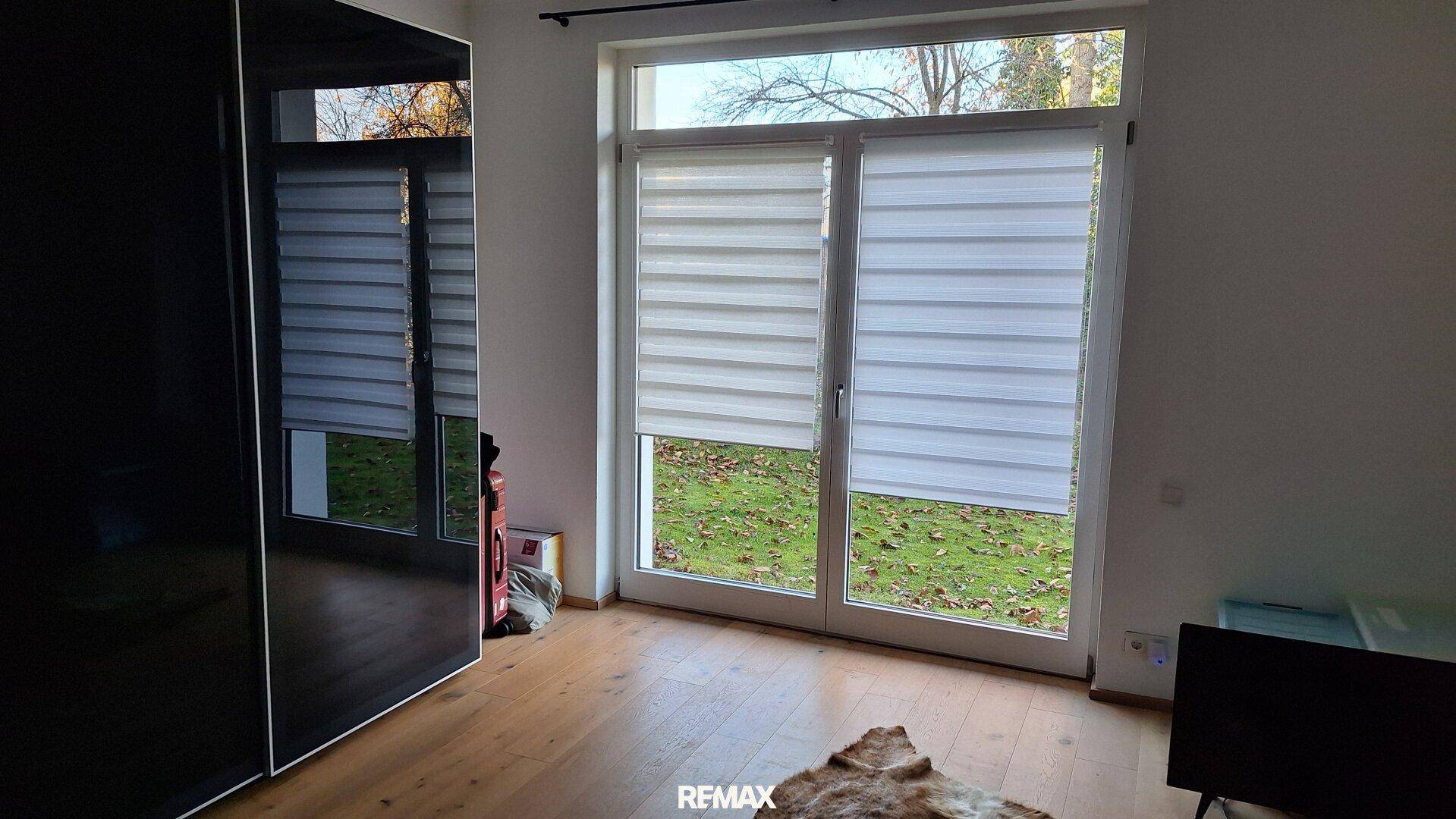 Schlafzimmer mit großem Fenster und Zugang zum Garten, ausgestattet mit modernen Rollos.