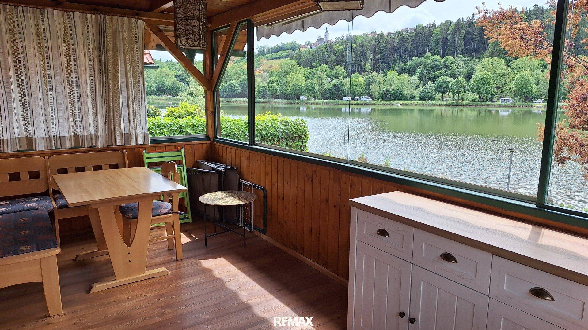 Gemütlicher Wintergarten mit Esstisch und Panoramablick auf den See und die umliegende Natur.