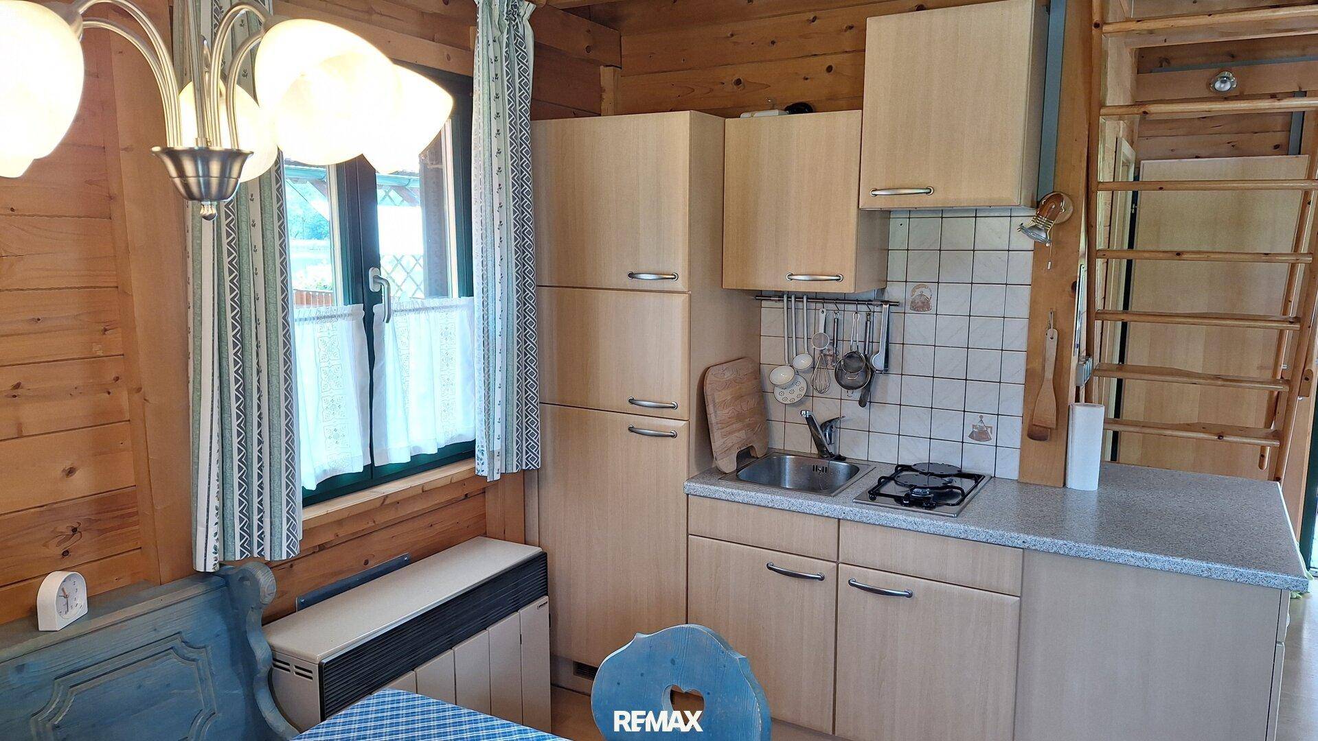 Kleine, funktionale Küche mit Holzschränken, Gasherd und Blick ins Grüne durch das Fenster.