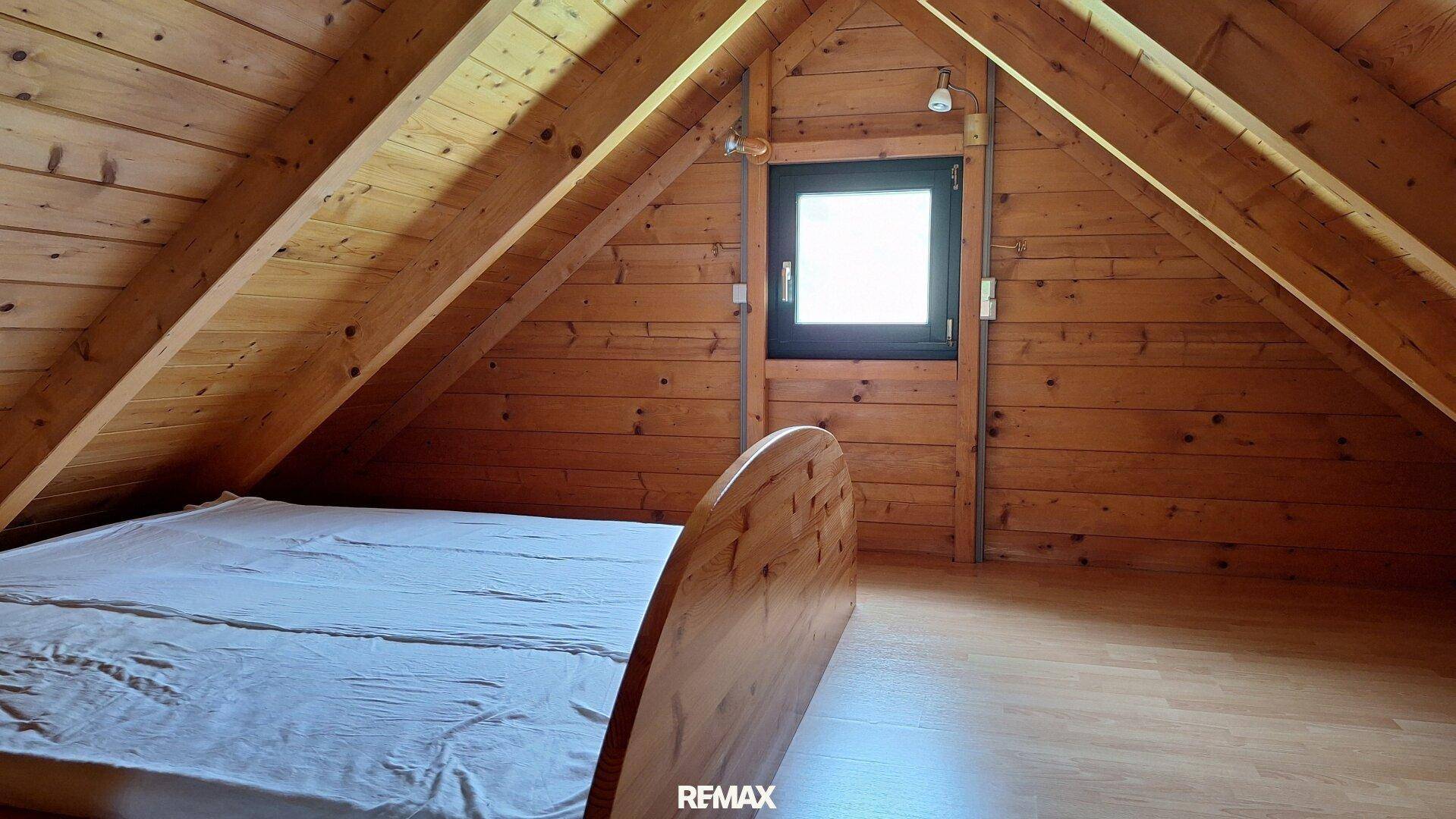 Schlafbereich im Dachgeschoss mit Holzwänden, sichtbaren Balken und schrägen Decken.
