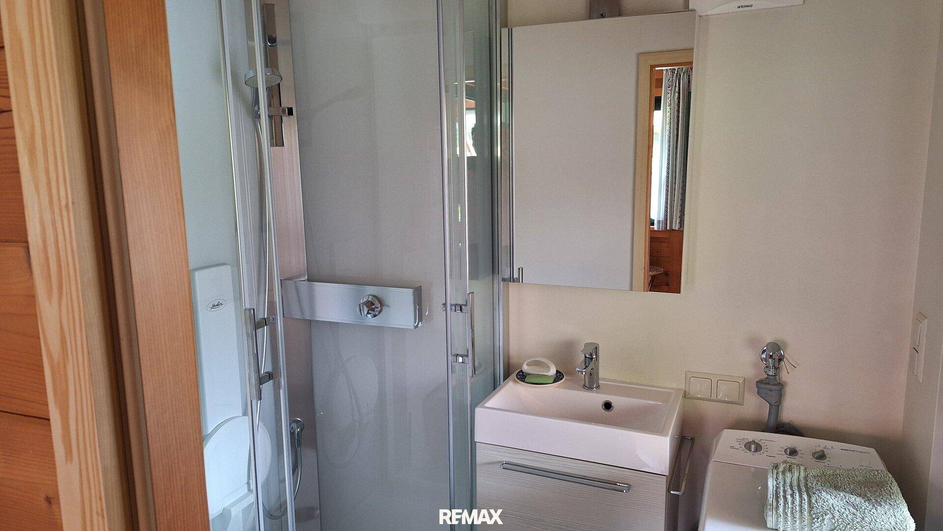 Modernes Badezimmer mit Duschkabine, Waschbecken und integrierter Waschmaschine.