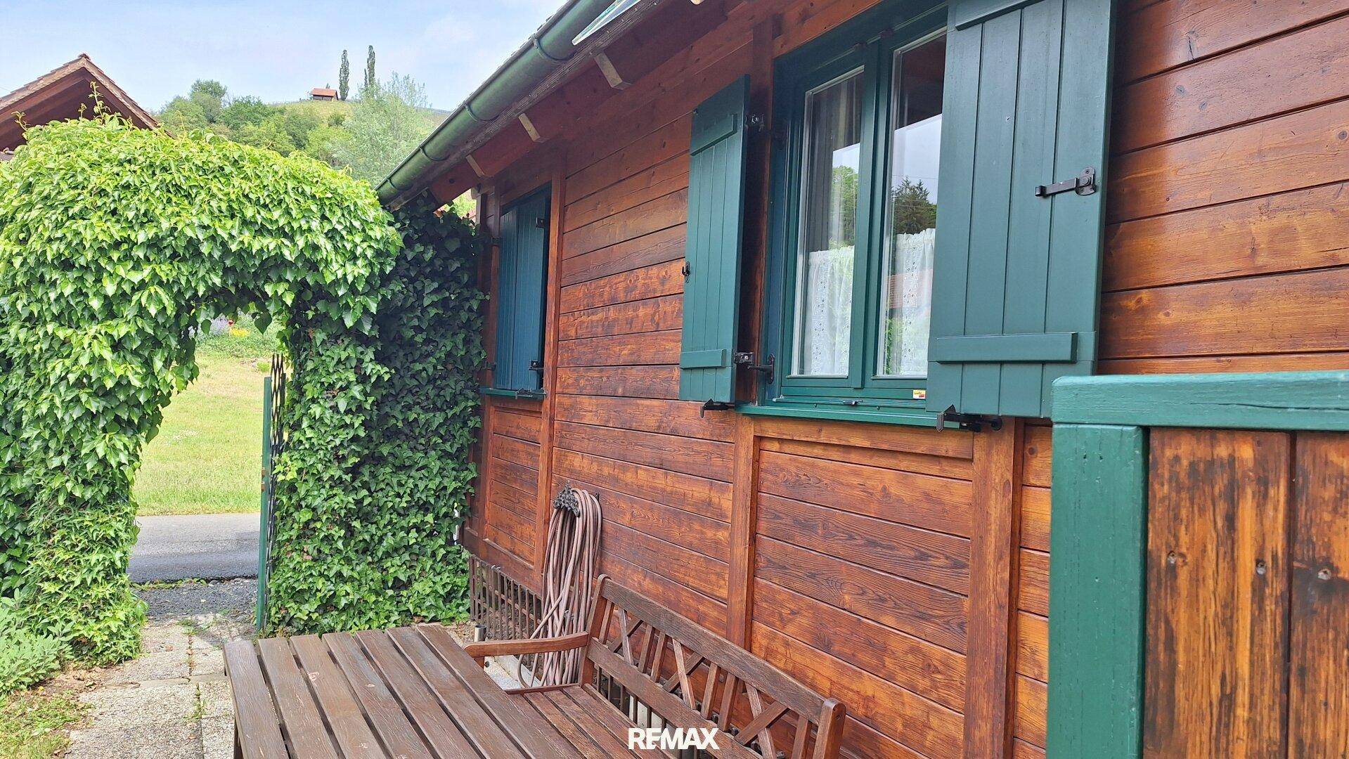 Seitenansicht des Holzhauses mit grünen Fensterläden und einer kleinen Holzbank.