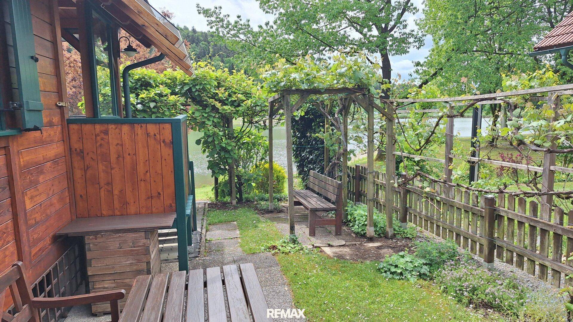 Gepflegter Gartenbereich mit Sitzbank, Holzzaun und idyllischem Seeblick.