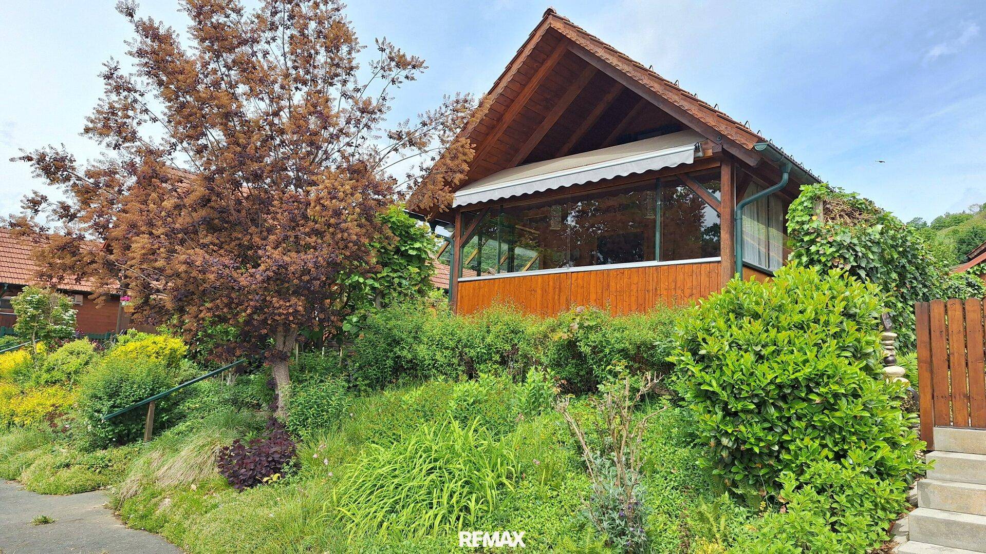 Charmantes Holzhaus mit Satteldach und gepflegtem Gartenbereich, umgeben von üppigem Grün.
