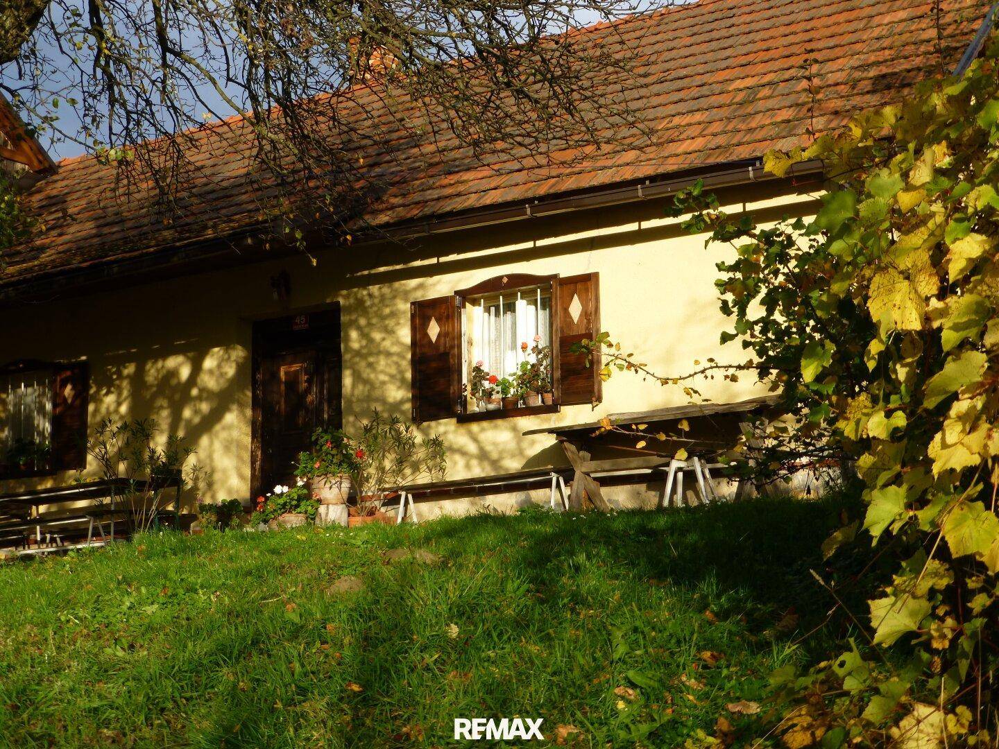 Altes Haus mit rustikalen Holzfensterläden und einer sonnigen Rasenfläche mit Sitzbänken davor.