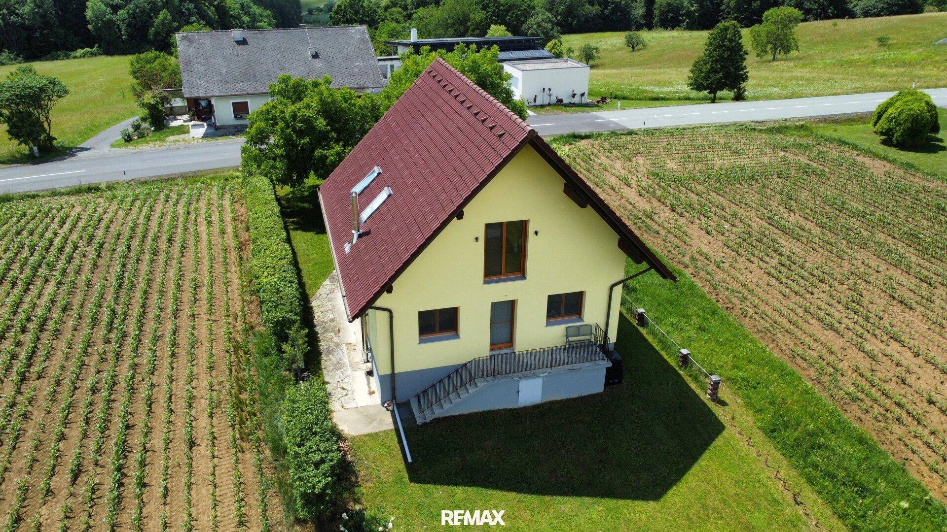 Rückansicht des gelben Einfamilienhauses mit rotem Dach, Dachfenstern und angrenzenden Feldern.